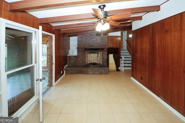 unfurnished living room featuring a brick fireplace, beam ceiling, ceiling fan, and wood walls