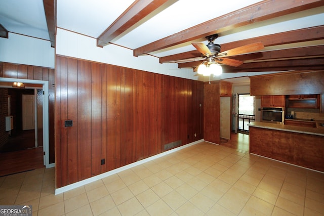 kitchen with light tile patterned flooring, wood walls, oven, ceiling fan, and beam ceiling