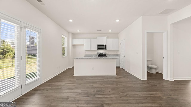 kitchen featuring white cabinetry, light stone counters, a center island with sink, appliances with stainless steel finishes, and dark hardwood / wood-style flooring