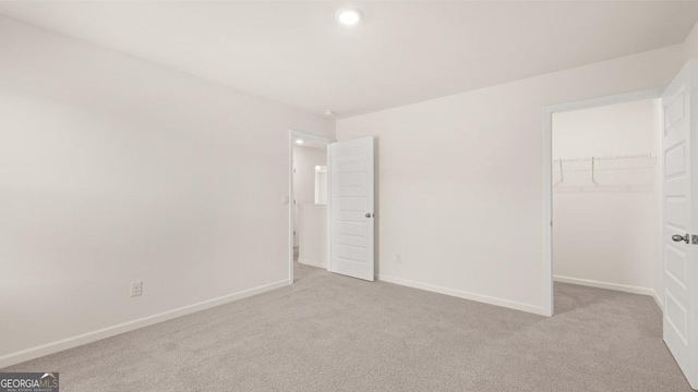 unfurnished bedroom with a spacious closet, light colored carpet, and a closet