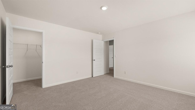 unfurnished bedroom with a spacious closet, light colored carpet, and a closet