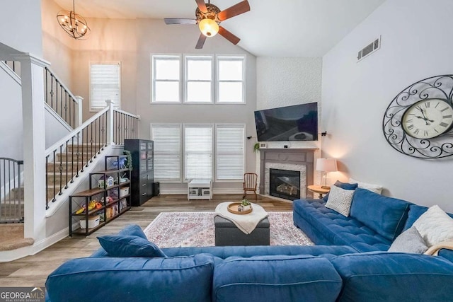 living room with a towering ceiling, wood-type flooring, and ceiling fan with notable chandelier