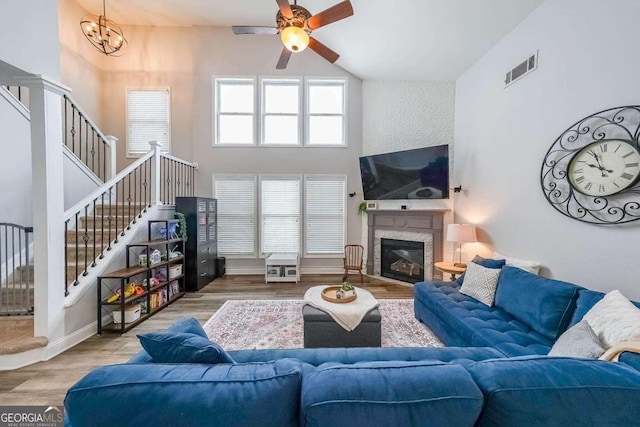living room featuring ceiling fan with notable chandelier, hardwood / wood-style floors, and a high ceiling