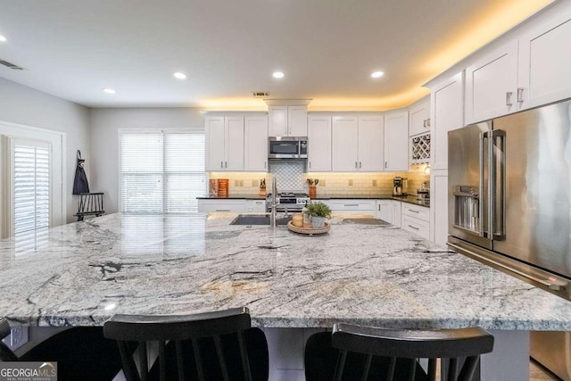 kitchen with stainless steel appliances, white cabinetry, light stone counters, and a kitchen breakfast bar