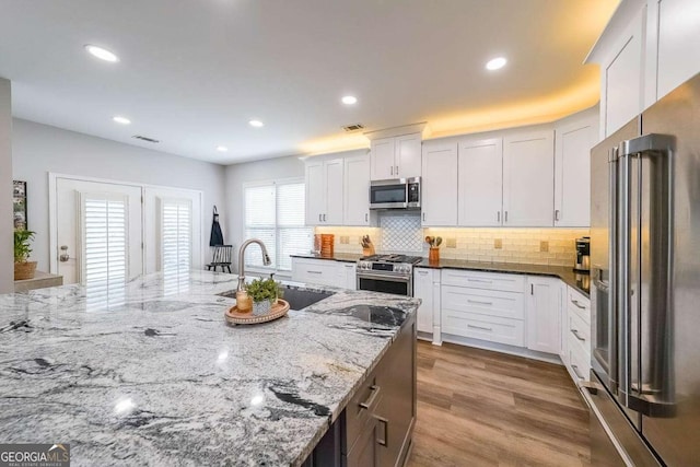 kitchen featuring hardwood / wood-style floors, sink, dark stone countertops, white cabinets, and high end appliances