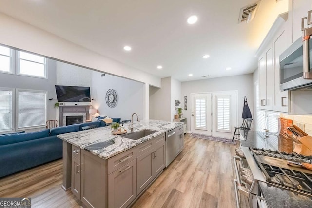 kitchen with sink, backsplash, stainless steel appliances, a center island with sink, and light wood-type flooring