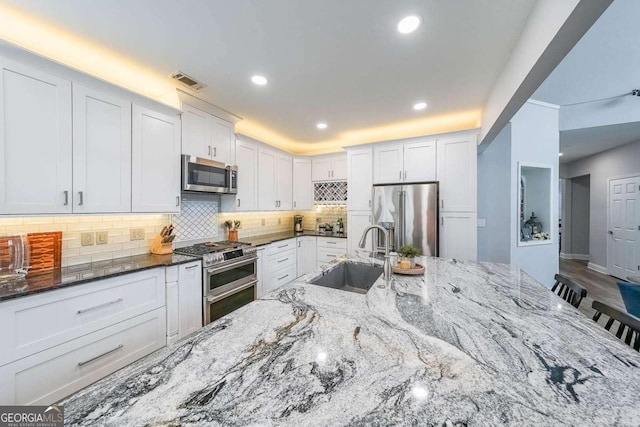 kitchen featuring appliances with stainless steel finishes, sink, white cabinets, and dark stone counters