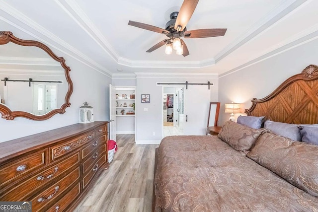 bedroom with ornamental molding, ceiling fan, a tray ceiling, a barn door, and light wood-type flooring