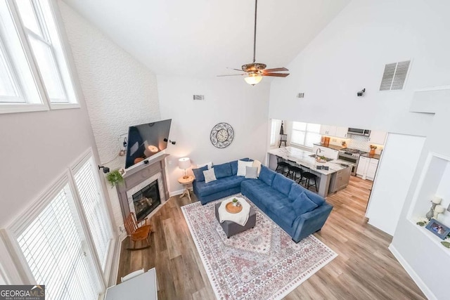 living room with ceiling fan, high vaulted ceiling, and light hardwood / wood-style floors