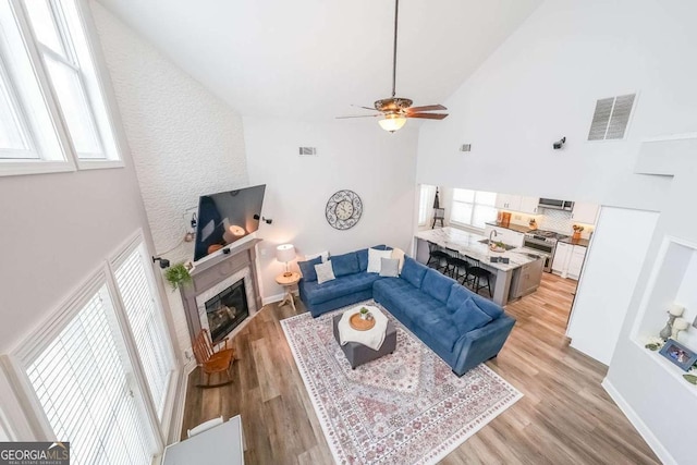 living room featuring ceiling fan, high vaulted ceiling, and light hardwood / wood-style flooring