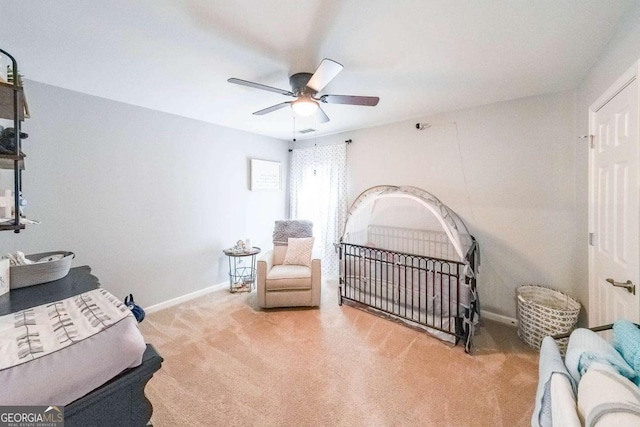 carpeted bedroom with a crib and ceiling fan