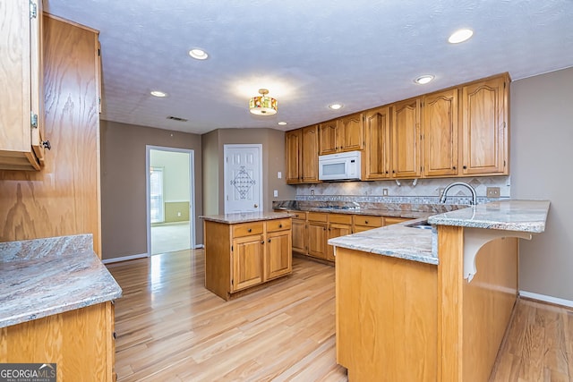 kitchen featuring sink, gas cooktop, backsplash, light stone counters, and kitchen peninsula