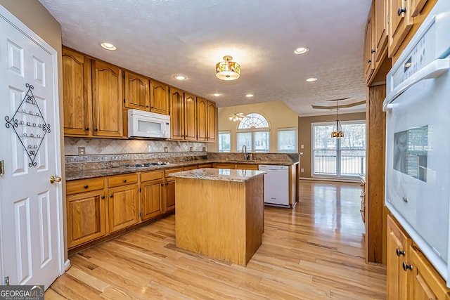 kitchen with sink, light wood-type flooring, hanging light fixtures, a center island, and white appliances