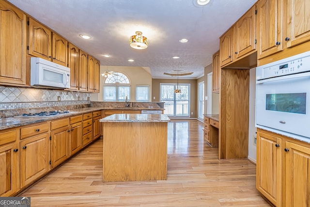 kitchen with sink, a kitchen island, pendant lighting, white appliances, and backsplash