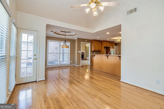 unfurnished living room featuring ceiling fan, a raised ceiling, sink, and light hardwood / wood-style flooring