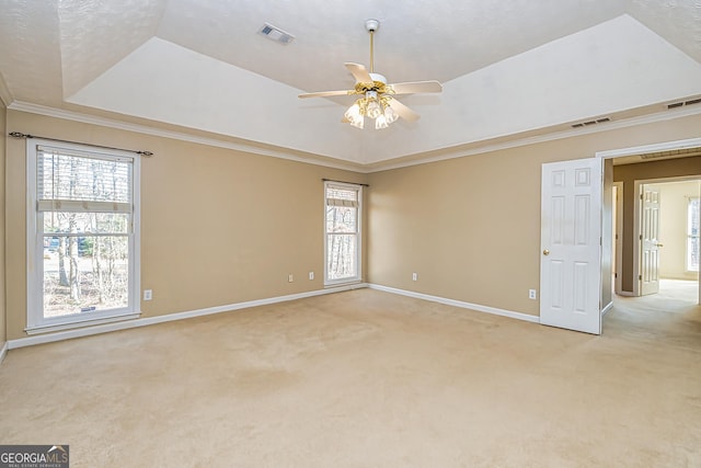 empty room featuring ornamental molding, light colored carpet, a raised ceiling, and a healthy amount of sunlight