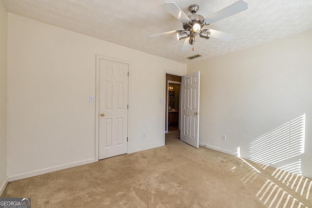 unfurnished bedroom with ceiling fan, light carpet, and a textured ceiling