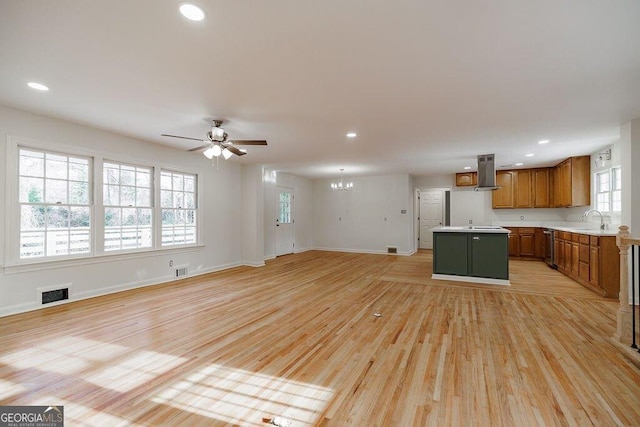 unfurnished living room with sink, ceiling fan with notable chandelier, and light hardwood / wood-style flooring