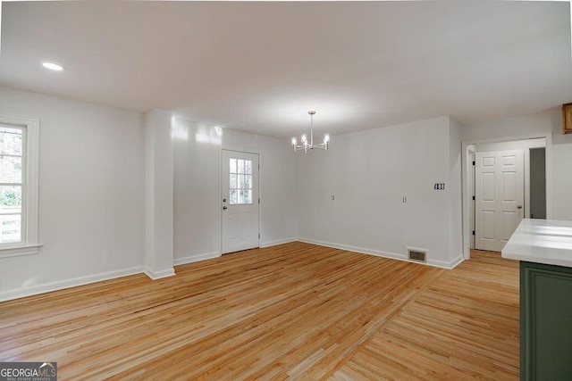 unfurnished room with a chandelier and light wood-type flooring