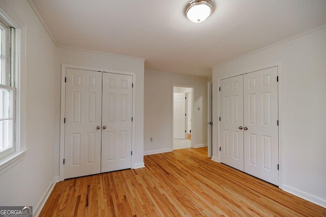 unfurnished bedroom with crown molding, two closets, and light wood-type flooring