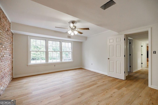 empty room featuring ceiling fan, brick wall, and light hardwood / wood-style floors