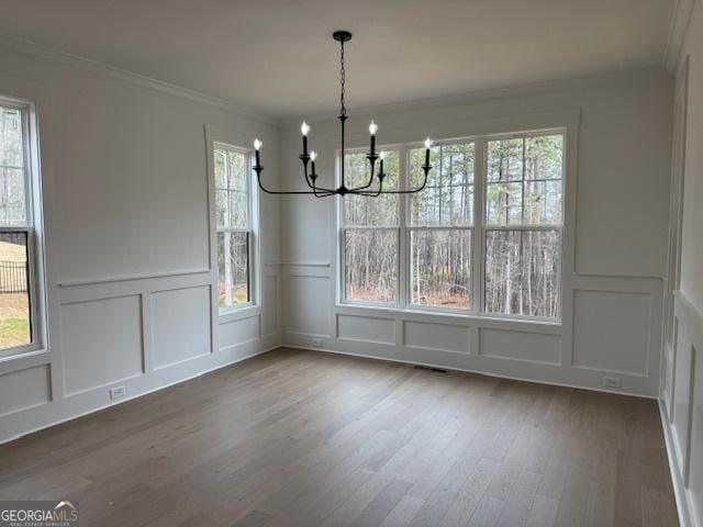 unfurnished dining area featuring crown molding, wood finished floors, a notable chandelier, and a decorative wall