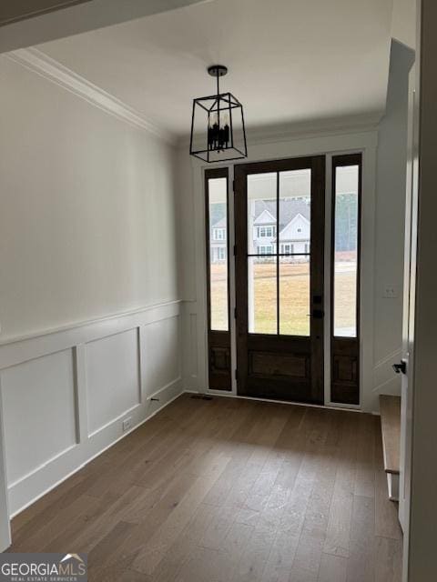 entryway featuring a decorative wall, hardwood / wood-style floors, a notable chandelier, and ornamental molding