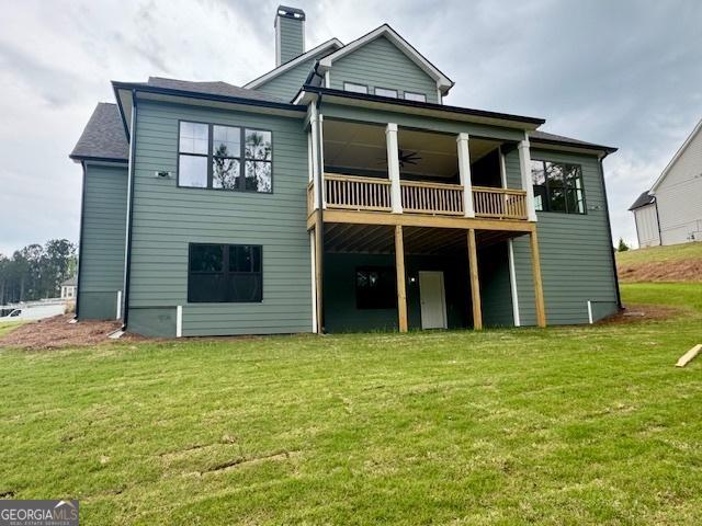 rear view of property featuring a ceiling fan, a lawn, a chimney, and a deck