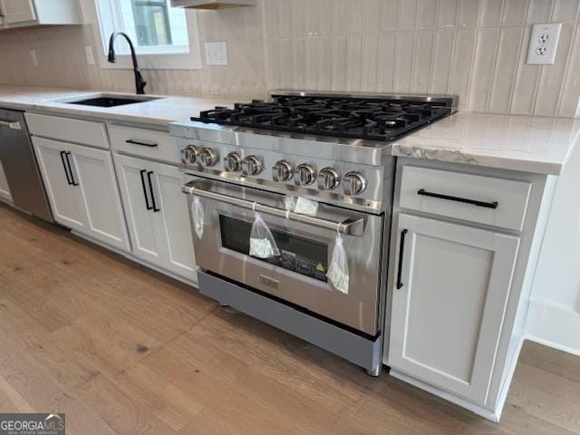 kitchen with white cabinets, a sink, light wood-type flooring, tasteful backsplash, and appliances with stainless steel finishes