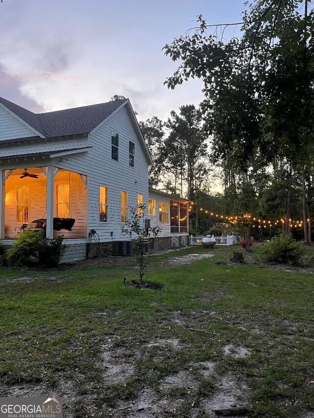 182 Rogers St, Hazlehurst, GA 31539 - back of property at dusk with ceiling fan, a sunroom, a yard, cooling unit, and a shingled roof