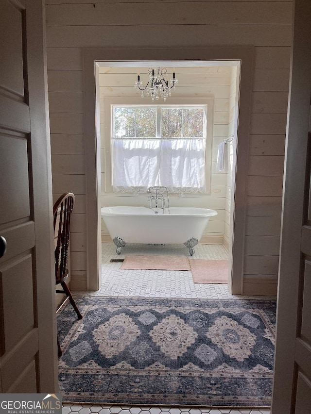 bathroom with tile patterned flooring, a washtub, an inviting chandelier, and wood walls