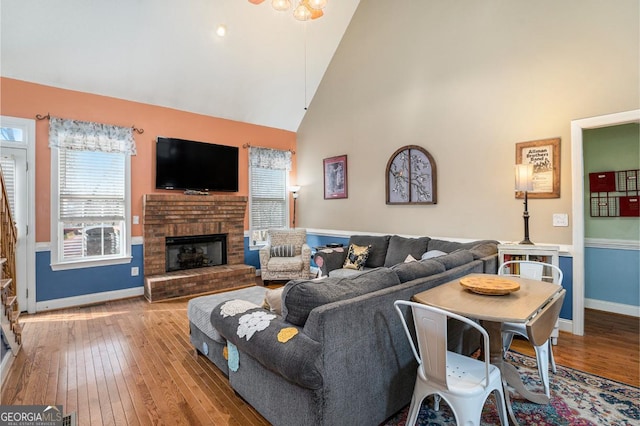 living room featuring high vaulted ceiling, a brick fireplace, and light wood-type flooring