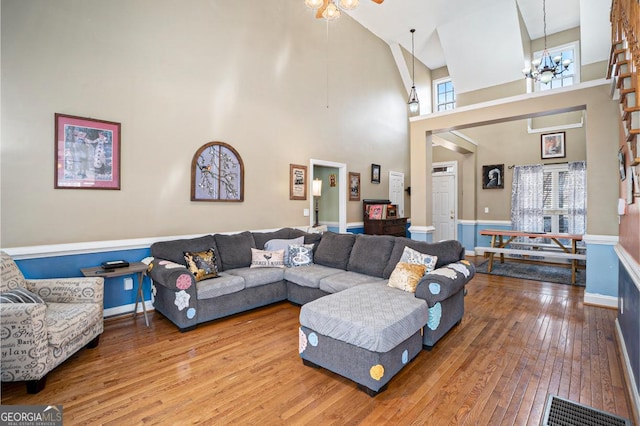 living room with a towering ceiling, wood-type flooring, and ceiling fan with notable chandelier