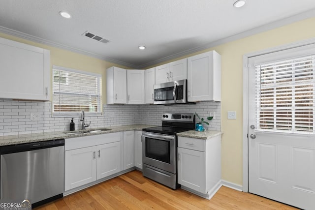 kitchen featuring sink, white cabinets, ornamental molding, light hardwood / wood-style floors, and stainless steel appliances