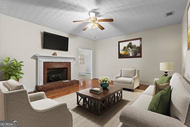 living area featuring a textured ceiling, a brick fireplace, light wood-style floors, and ceiling fan