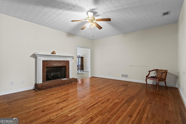 unfurnished living room featuring wood finished floors, baseboards, visible vents, a fireplace, and ceiling fan