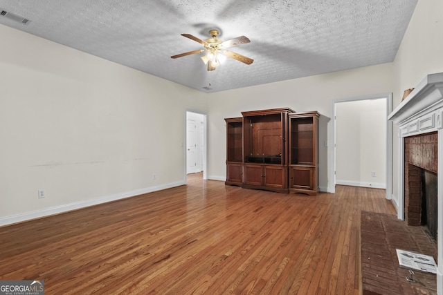 unfurnished living room featuring baseboards, visible vents, a fireplace, ceiling fan, and wood-type flooring