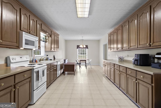 kitchen with decorative light fixtures, light floors, light countertops, white appliances, and a sink