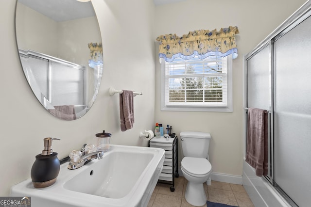 full bath featuring tile patterned flooring, baseboards, bath / shower combo with glass door, toilet, and a sink