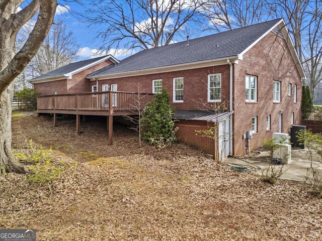 back of house featuring a patio, brick siding, roof with shingles, and a deck