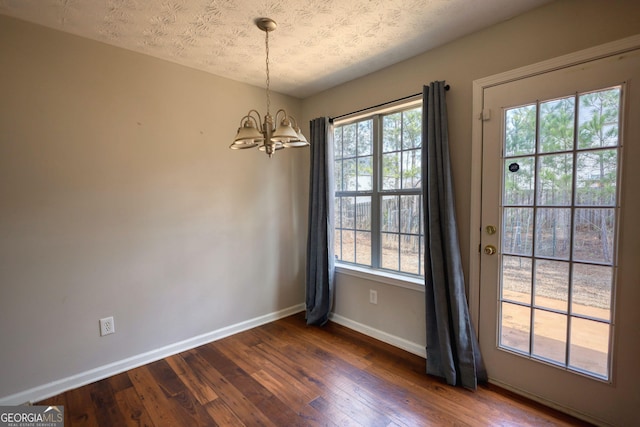 unfurnished room with a notable chandelier, dark hardwood / wood-style floors, and a textured ceiling