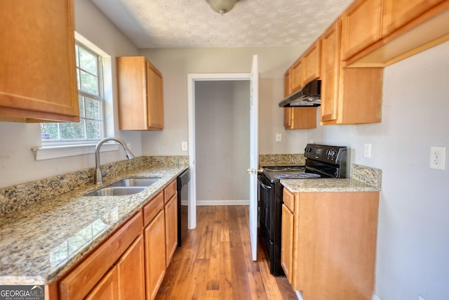 kitchen featuring black appliances, sink, light stone counters, light hardwood / wood-style floors, and a textured ceiling