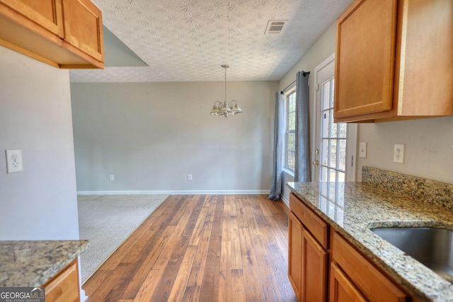 kitchen with an inviting chandelier, dark hardwood / wood-style floors, light stone countertops, a textured ceiling, and decorative light fixtures