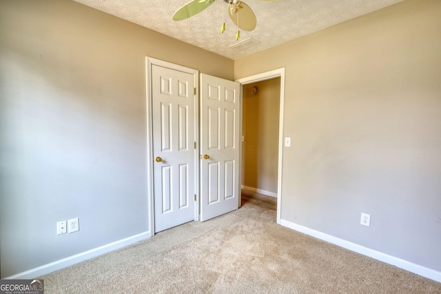 unfurnished bedroom with ceiling fan, light colored carpet, a closet, and a textured ceiling