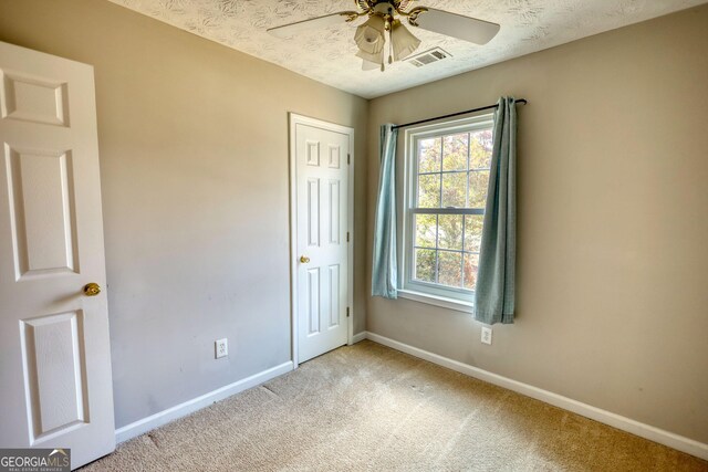 unfurnished bedroom featuring ceiling fan, light colored carpet, and a textured ceiling