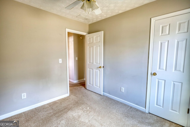 unfurnished bedroom with ceiling fan, light colored carpet, and a textured ceiling