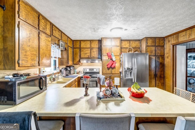 kitchen with a kitchen bar, sink, a textured ceiling, kitchen peninsula, and stainless steel appliances