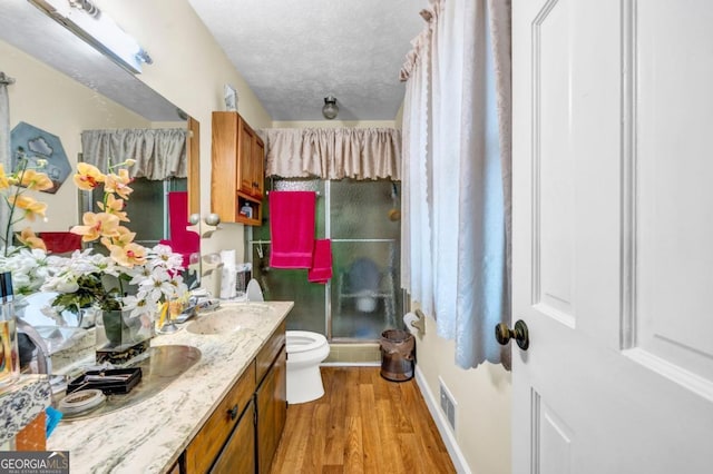 bathroom with hardwood / wood-style floors, vanity, walk in shower, toilet, and a textured ceiling