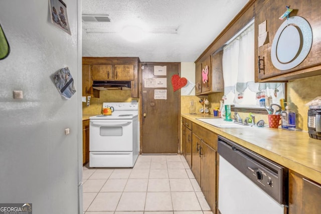 kitchen with sink, light tile patterned floors, a textured ceiling, and white appliances