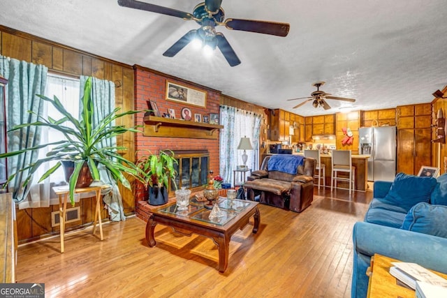 living room featuring a brick fireplace, light hardwood / wood-style floors, a textured ceiling, and wood walls